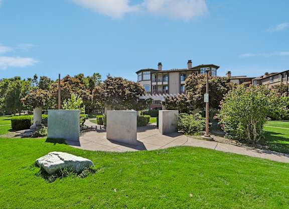 A green lawn with a large rock in the foreground and a building in the background.