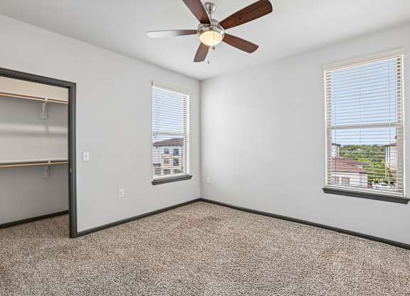 A room with a ceiling fan and two windows.