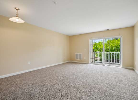 A room with a carpeted floor and a sliding glass door leading to a green outdoor area.