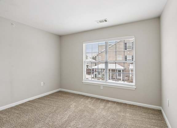 A room with a carpeted floor and a window showing a building outside.