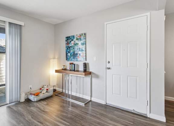 A room with a white door, a table with a lamp and a painting on the wall.