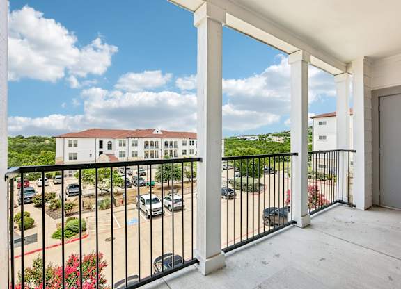 A balcony with a black railing overlooks a parking lot and buildings.
