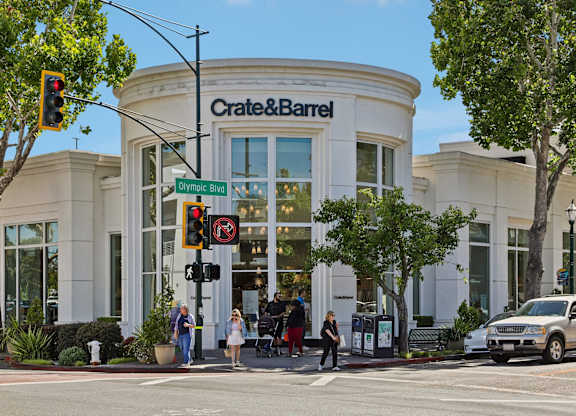 A Crate & Barrel store is shown with people walking by and a car parked in front.