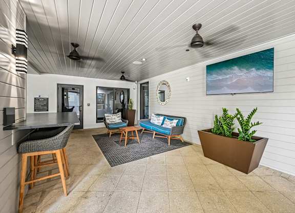 A living room with a ceiling fan and a painting of a beach scene on the wall.