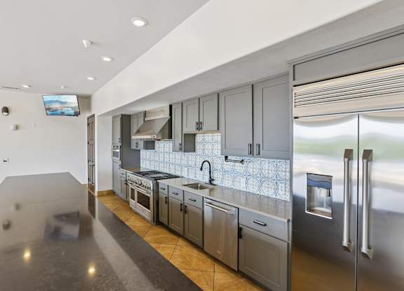 A modern kitchen with stainless steel appliances and a flat screen TV mounted on the wall.