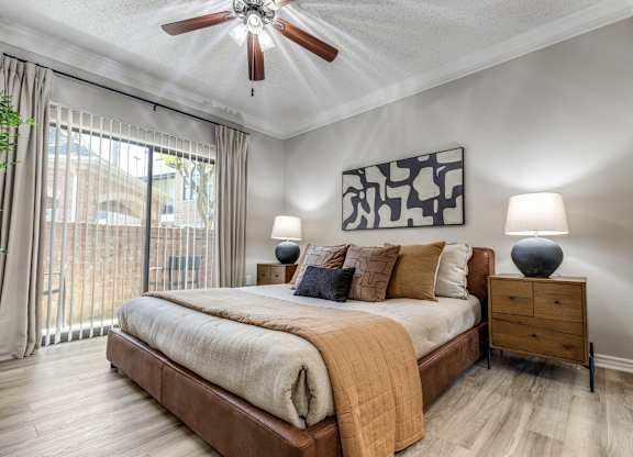 A bedroom with a bed, a ceiling fan, and a painting on the wall.