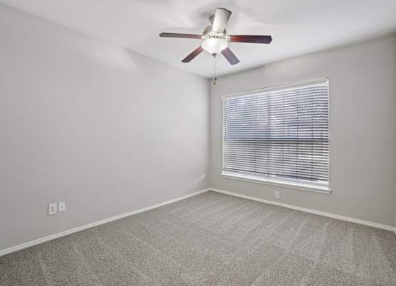 A room with a ceiling fan and a window with blinds.