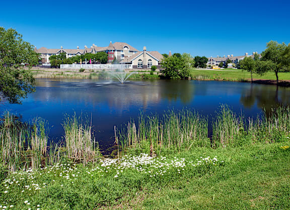 a pond with grass and flowers in front of a house