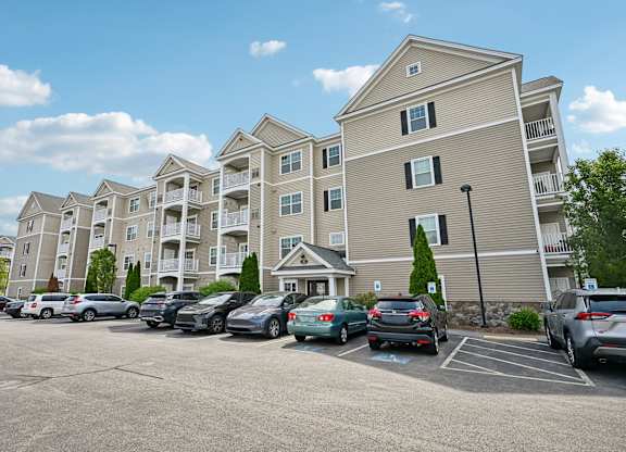 A parking lot in front of a large apartment building with cars parked.