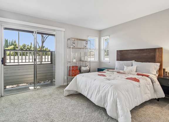 A bedroom with a large bed and a sliding glass door leading to a balcony.