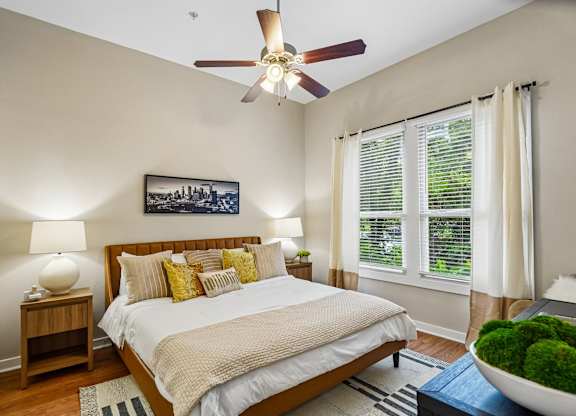 A bedroom with a large bed, a ceiling fan, and a painting on the wall.