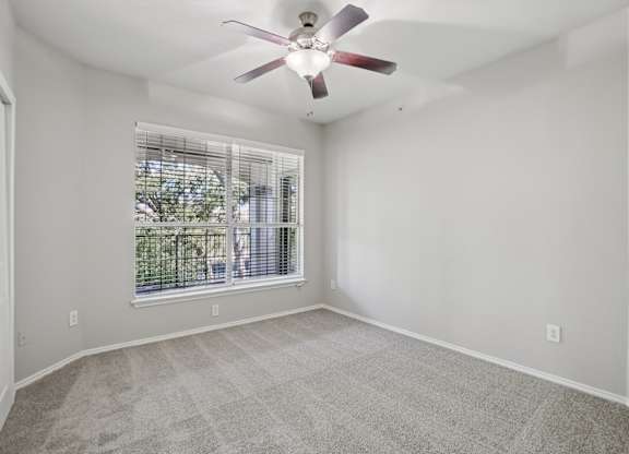 A room with a ceiling fan and a window with blinds.