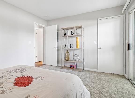 A white bedroom with a bed and a shelf with letters and bottles.