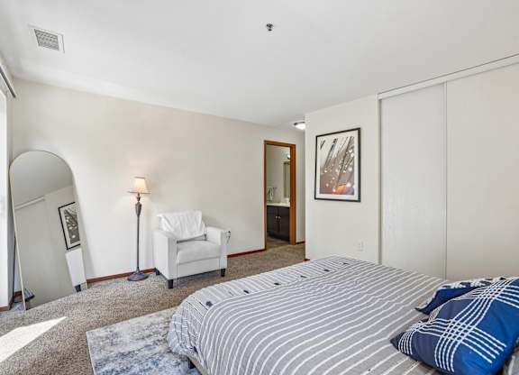 A bedroom with a bed, chair, and painting.