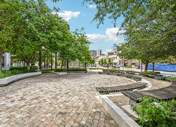 A park with a circular brick walkway surrounded by trees.