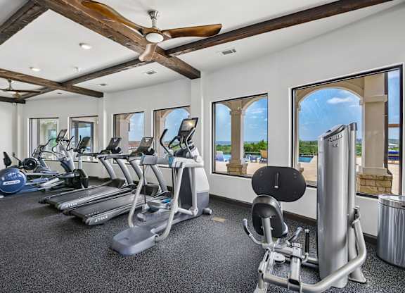 A gym with a row of treadmills and a fan.