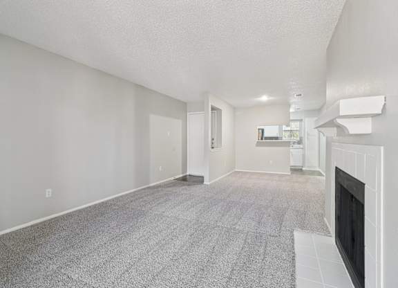A living room with a fireplace and a grey carpet.