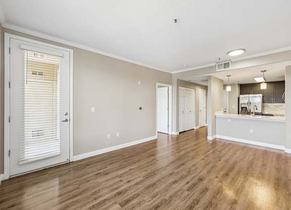 A room with wooden floors and a kitchen area in the background.