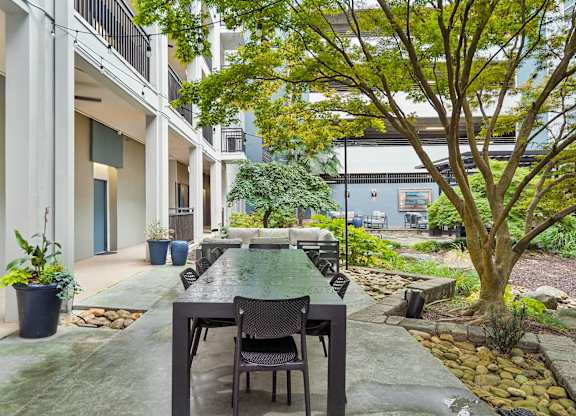 A patio with a table and chairs is surrounded by trees and plants.