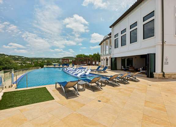 A pool with chairs and a building in the background.