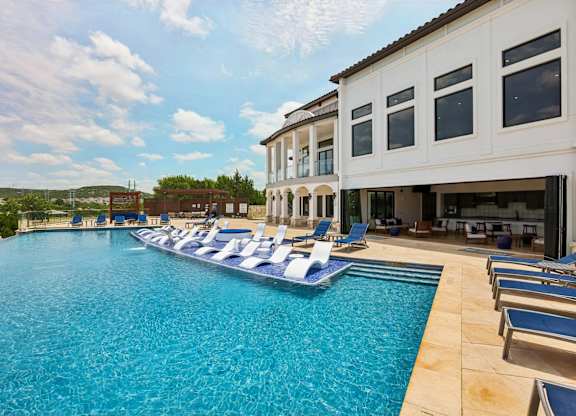 A large swimming pool with lounge chairs and a building in the background.
