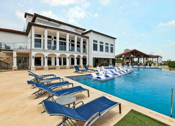 A pool with lounge chairs and a building in the background.