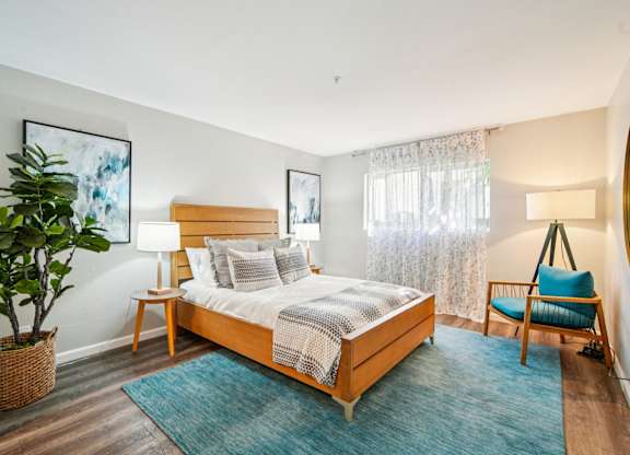 A bedroom with a bed, a chair, and a potted plant.