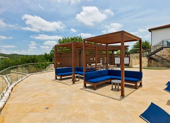 A wooden pavilion with blue seating is surrounded by a stone wall.