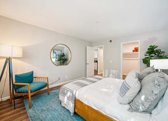 A bedroom with a bed, chair, and a mirror on the wall.