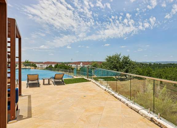 A pool area with a glass railing and chairs.