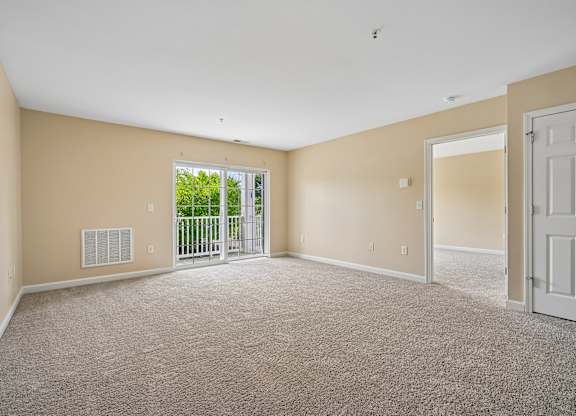 A spacious room with a carpeted floor and a sliding glass door leading to a balcony.