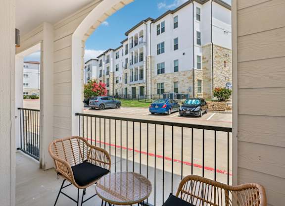 A balcony with a chair and table overlooking a parking lot.