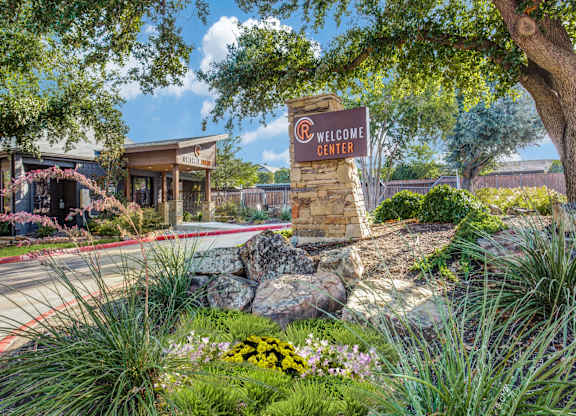 A welcome center sign is in front of a building with a landscaped area.