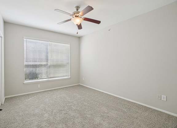 A room with a ceiling fan and a window with blinds.
