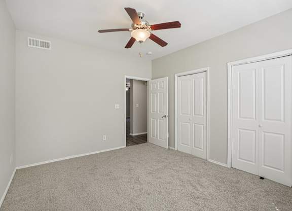 A room with a ceiling fan and three doors.