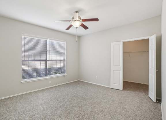 A room with a ceiling fan and a window with blinds.