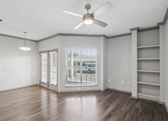 A room with a ceiling fan and a window with a view of a street.