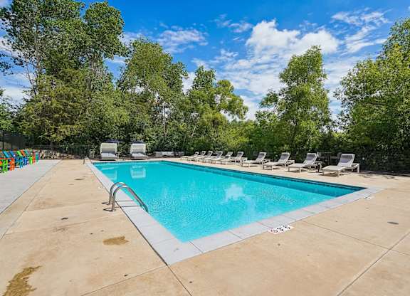 A large outdoor swimming pool surrounded by trees and lounge chairs.