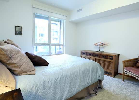 A bedroom with a bed, chair, and window.