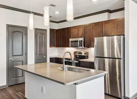 A kitchen with a stainless steel refrigerator and a white island with a sink.