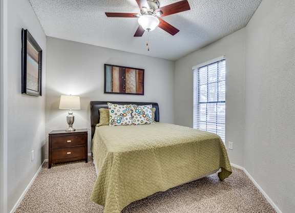 A bedroom with a bed, nightstand, and a ceiling fan.