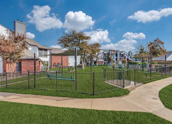 A park with a fence and a bench in front of a building.