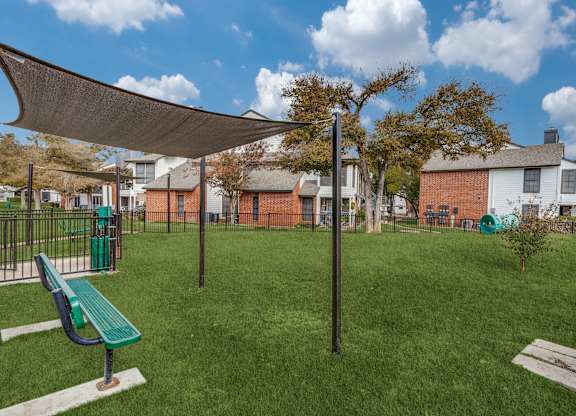 A park with a green bench and a green trash can.
