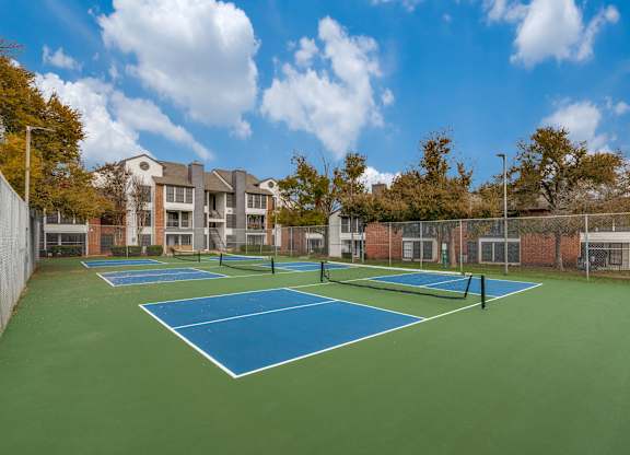 A tennis court surrounded by a fence and a building in the background.