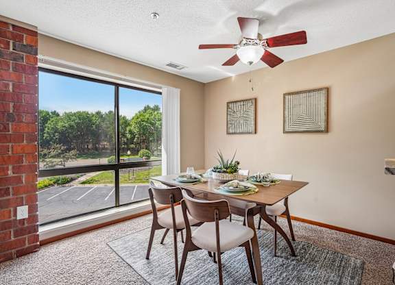 A dining room with a table set for two and a fan on the ceiling.