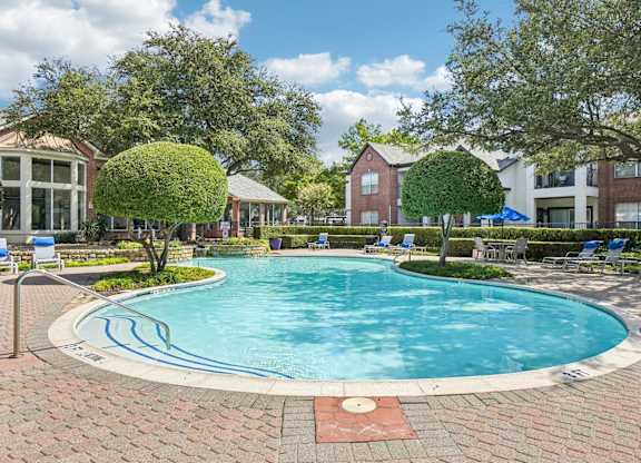 A large swimming pool surrounded by a brick patio and trees.