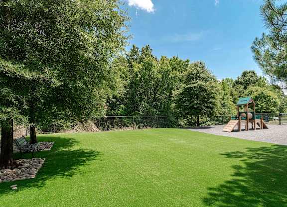 A playground with a green lawn and trees.