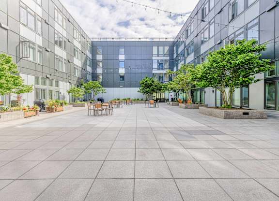 Green Lake, Seattle, WA, Apartments For Rent - Circa Green Lake - Courtyard With Picnic Tables And Chairs, Cafe Lights, Plants, Trees, And Surrounding Apartment Buildings.