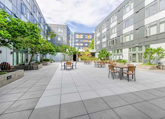 a courtyard with tables and chairs and trees and buildings in the background