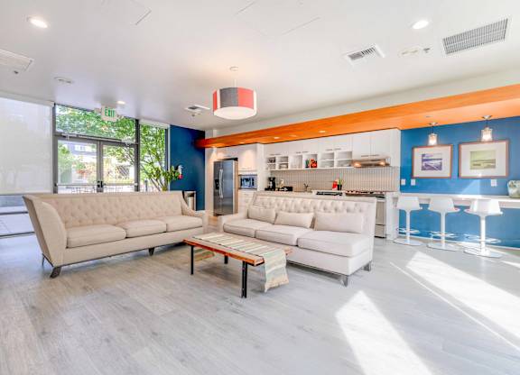 Apartments For Rent In Green Lake, Seattle, WA - Circa Green Lake - Resident Clubhouse With Hardwood Floor, Sofas, Kitchen, Counter with Seating Area, And Glass Doors Leading To Courtyard.